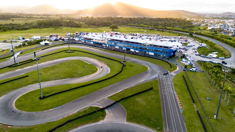 Top-down view of a high-speed 1:8 scale nitro RC car racing on an outdoor dirt track with blurred motion, orange safety barriers, and digital lap timer visible